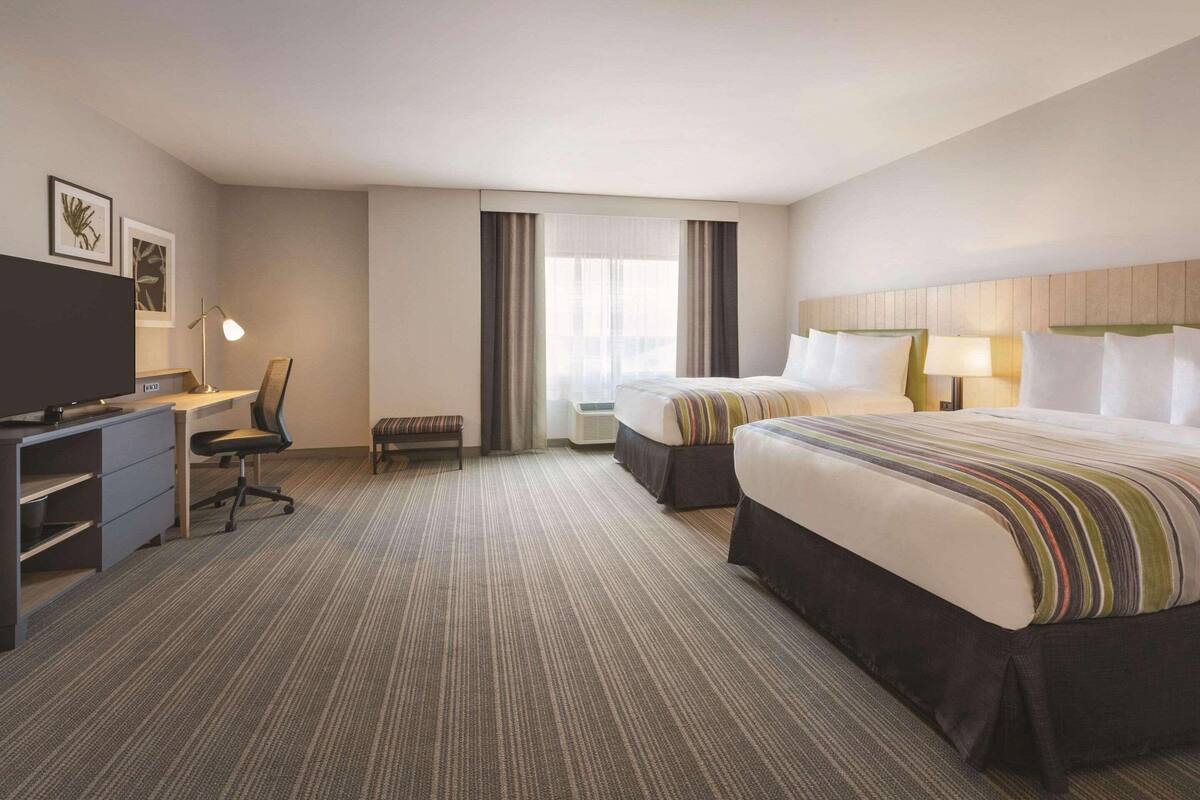 A hotel room with a large bed, a smaller bed, a desk with a chair, a television, and a window with curtains.