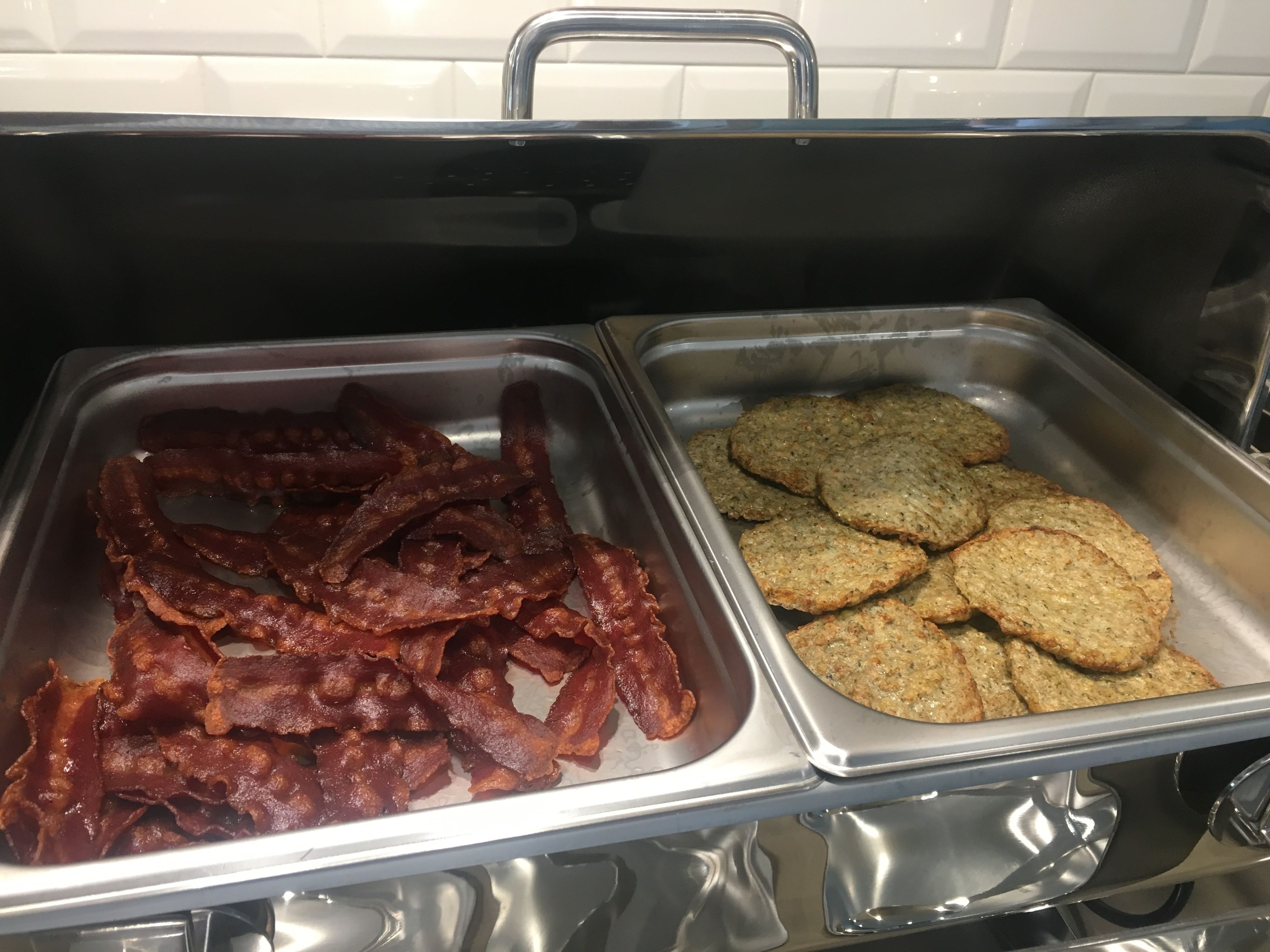 A buffet with two trays, one containing bacon and the other containing oatmeal cookies.