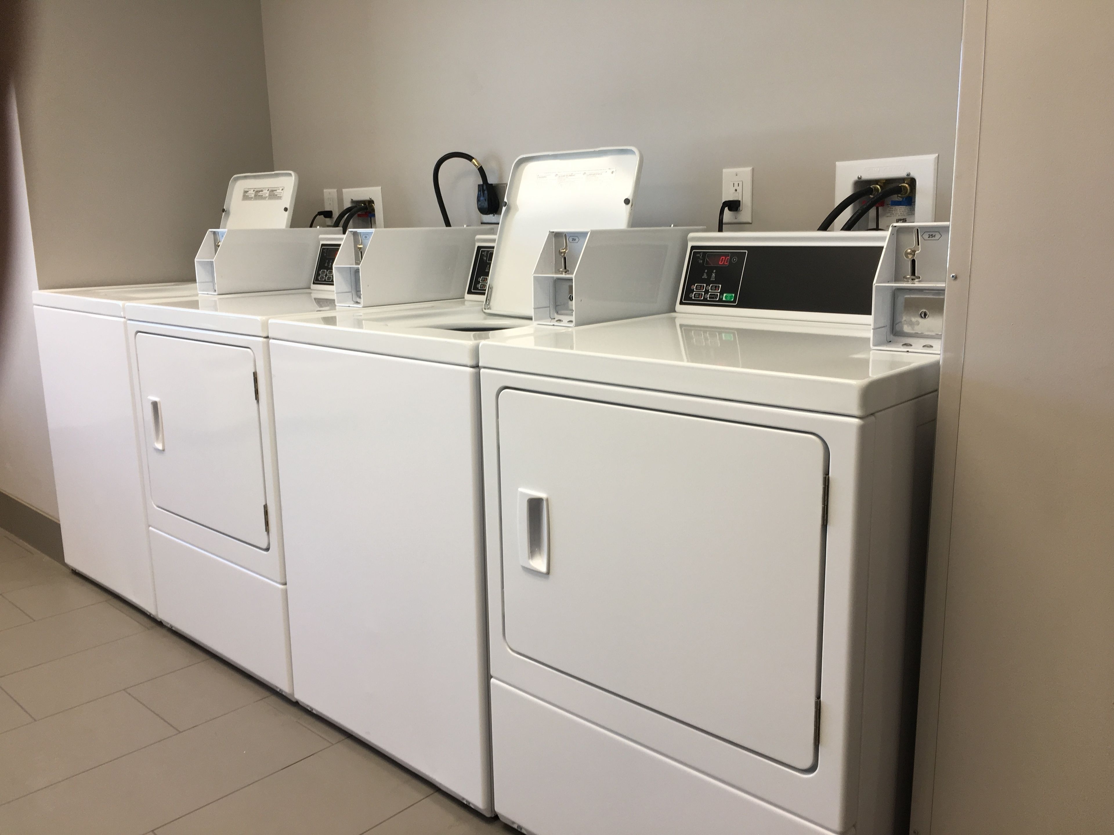 A row of white, modern, front-loading washers and dryers in a clean, tiled laundry room.