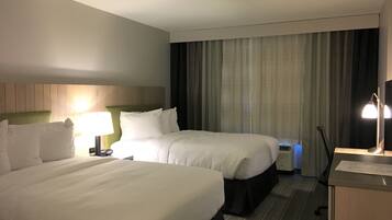 A hotel room with two beds, a desk, a lamp, and a window with curtains.