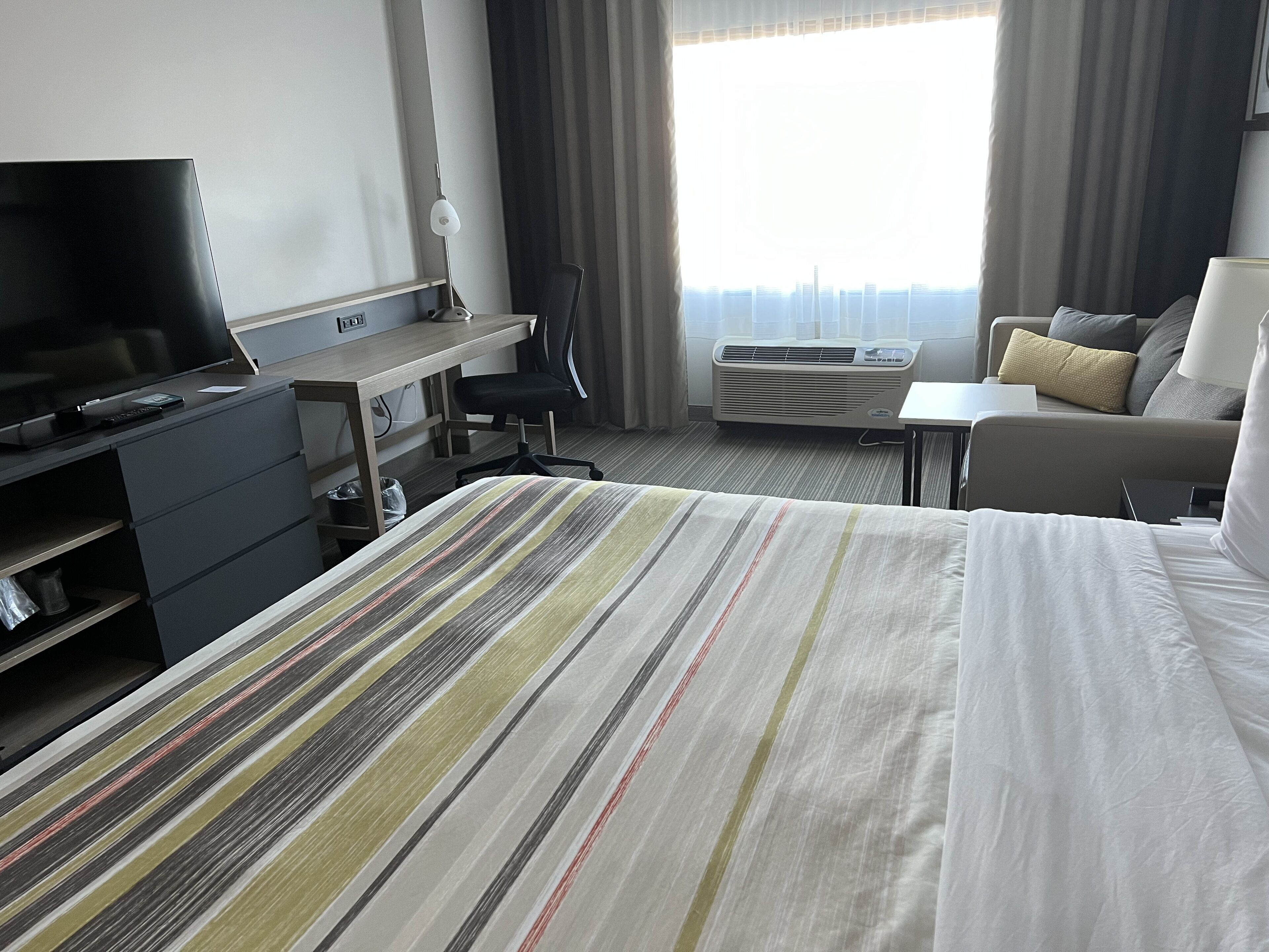 Ein Hotelzimmer mit Bett, Schreibtisch, Stuhl, Fernseher und einem Fenster mit Vorhängen.