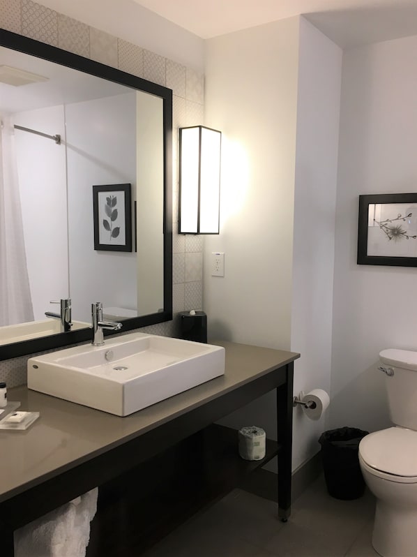 A modern bathroom with a large mirror, a white sink, a toilet, and a trash bin.