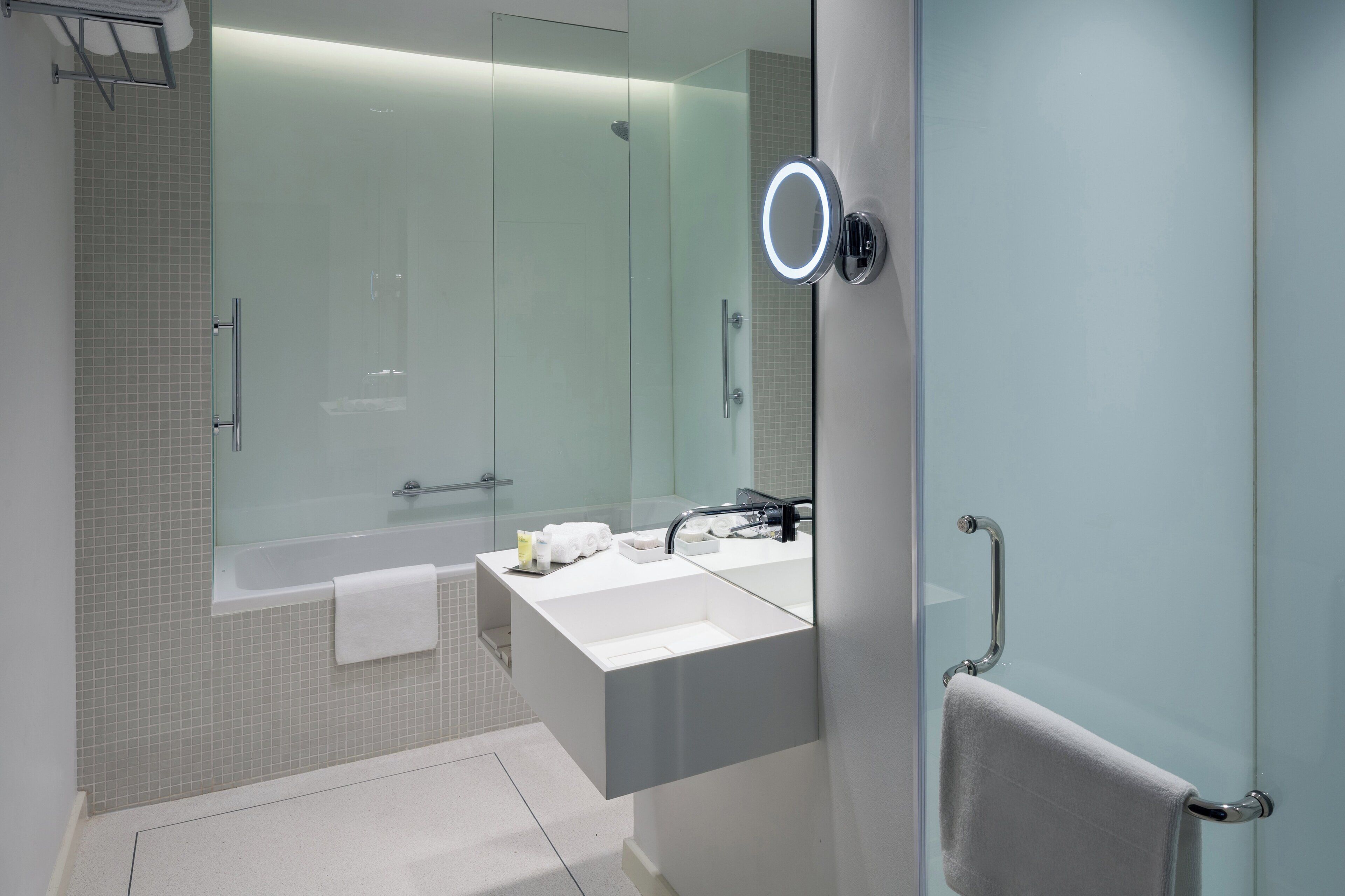 Un baño moderno con cabina de ducha de vidrio, tocador blanco y un perchero para toallas.