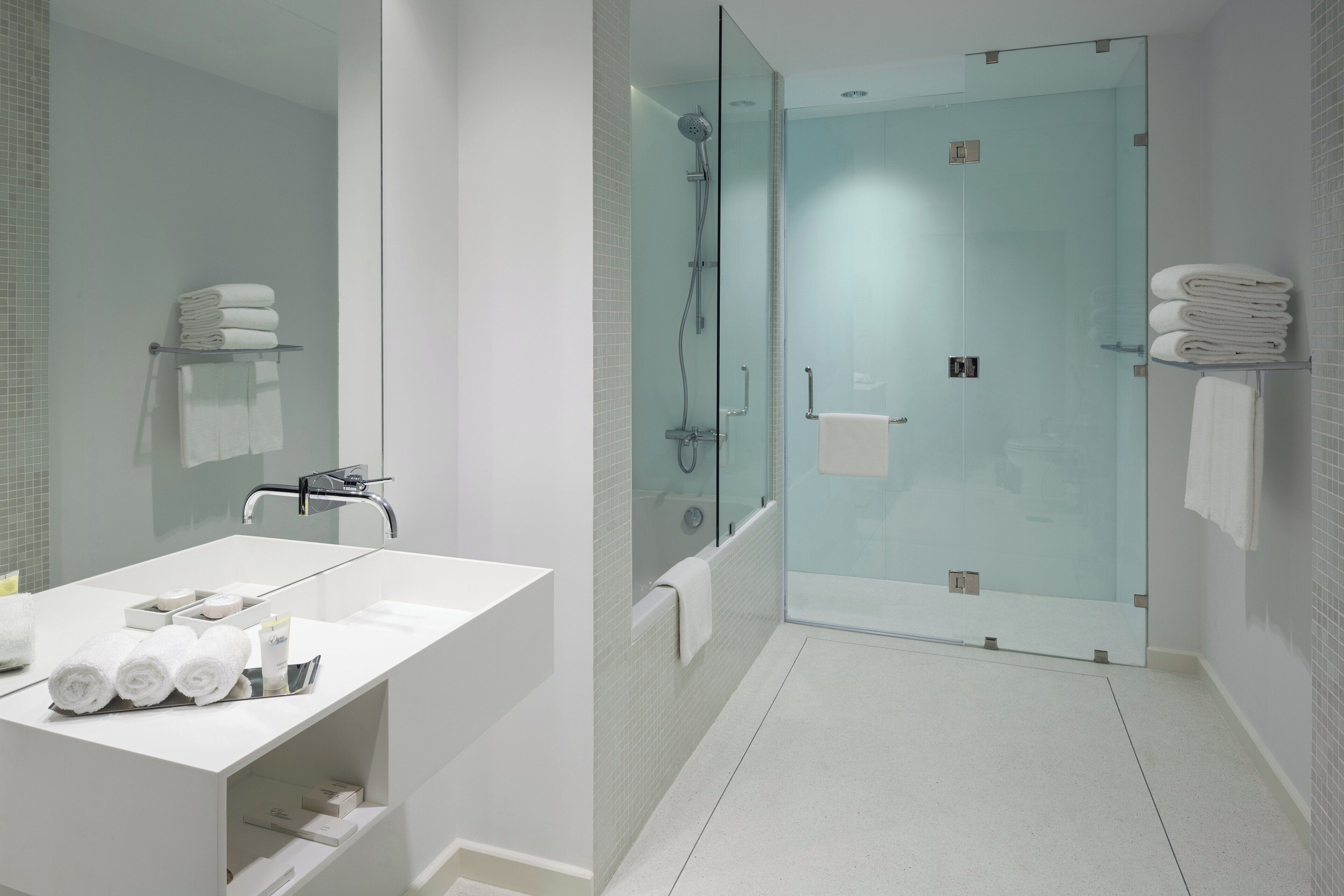 Un baño moderno con ducha envuelta en vidrio, un lavabo blanco y toallas ordenadas.