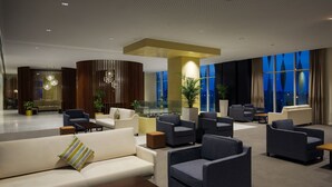 Um lobby moderno com áreas de estar, balcão de recepção e grandes janelas com vista para a cidade.