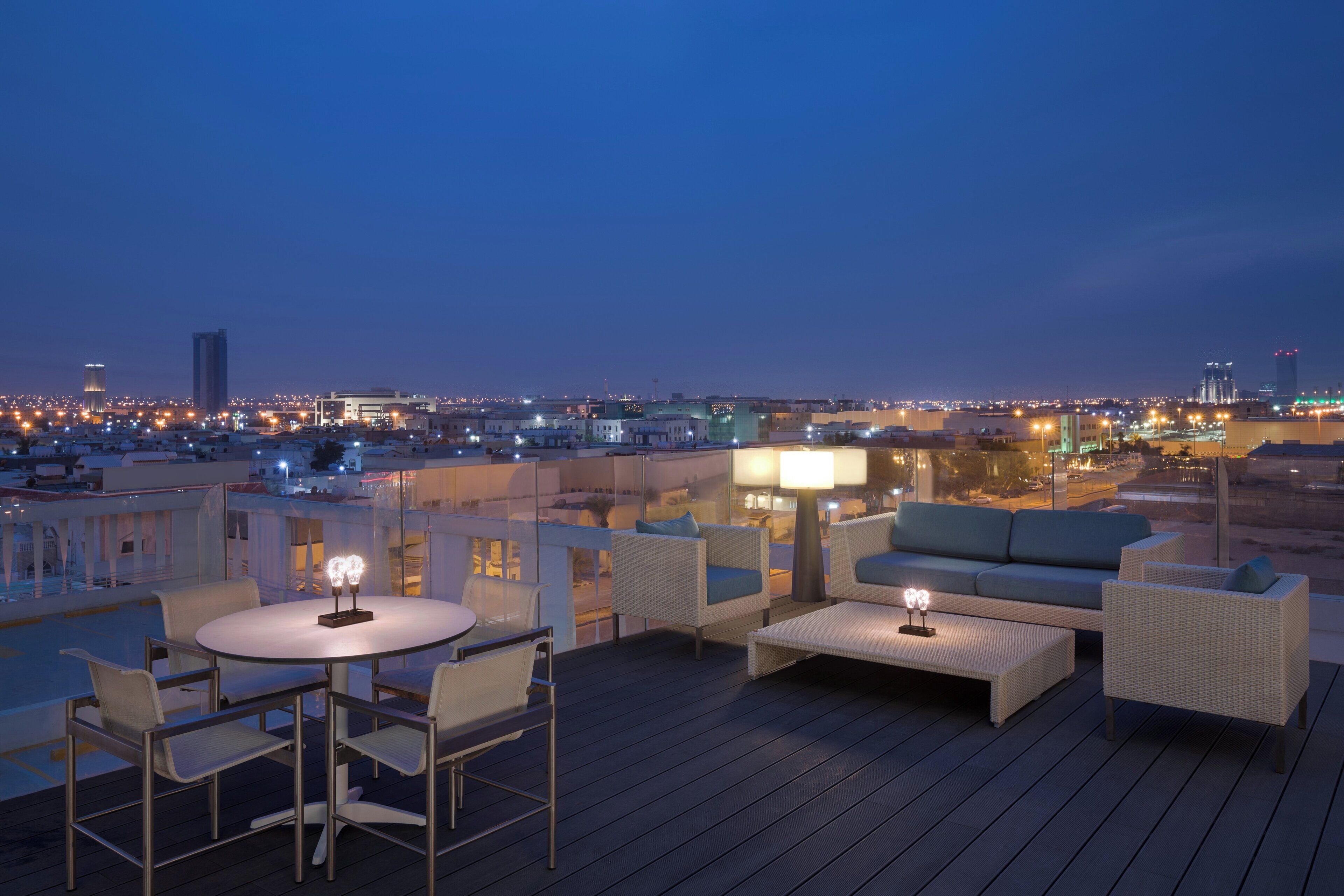 A rooftop terrace with outdoor seating and a city view at dusk.