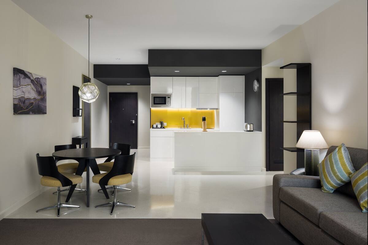 A modern living room with a dining area, a sofa, and a kitchen in the background.