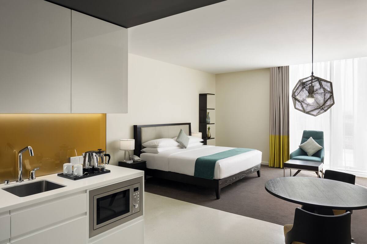 A hotel room with a bed, bedside table, lamp, and a dining area with a table and chairs.