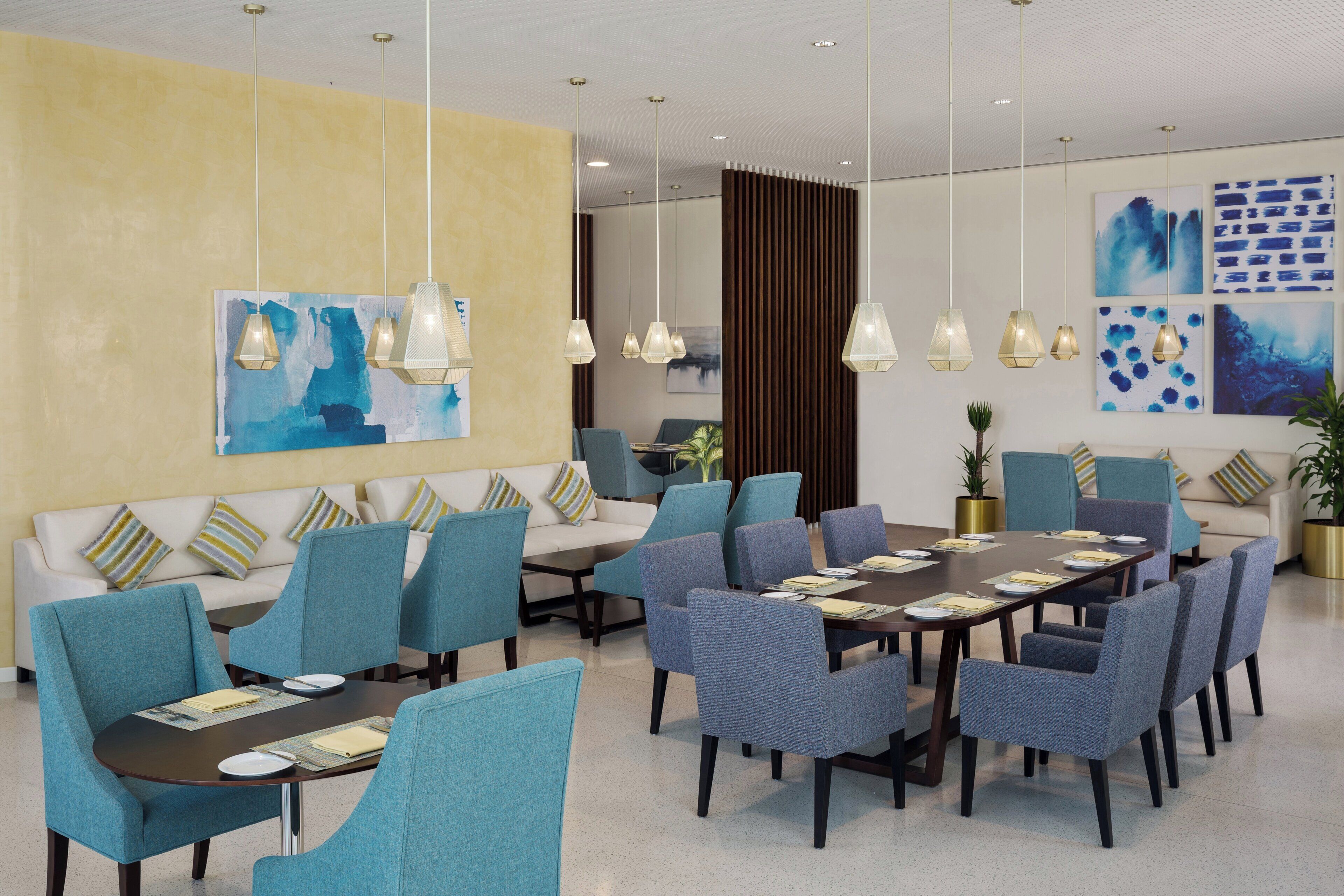Une chambre d’hôtel moderne dotée d’un coin repas, de canapés et d’œuvres d’art aux murs.