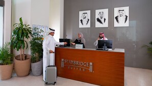 A reception desk at Staybridge Suites with three staff members, a large potted plant, and artwork on the wall.
