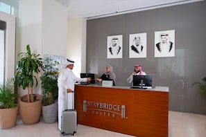 A reception desk at Staybridge Suites with three staff members, a large potted plant, and artwork on the wall. - Staybridge Suites Al Khobar by IHG (Al Khobar)