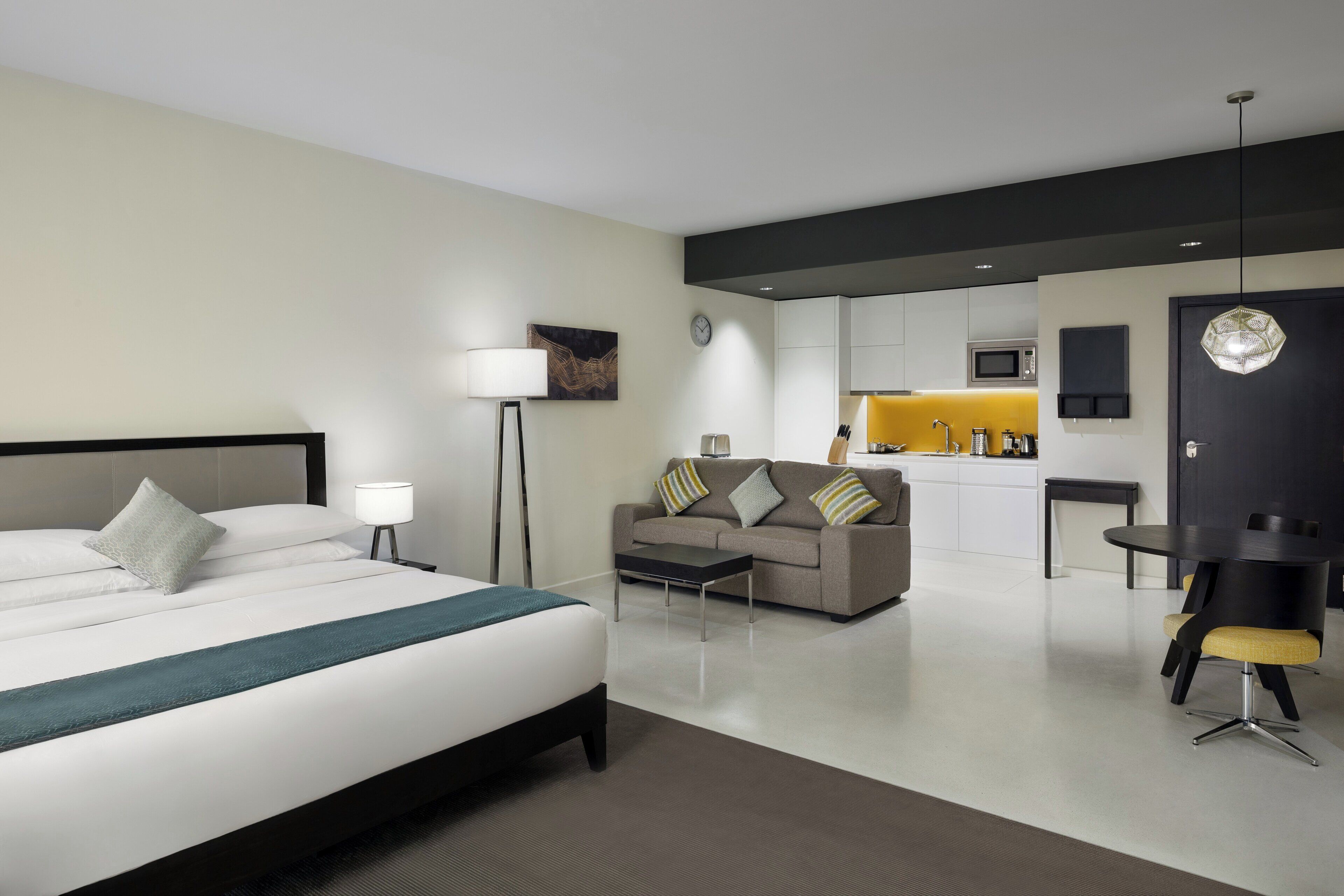 Habitación de hotel moderna con cama, sofá, mesa de comedor y zona de cocina.