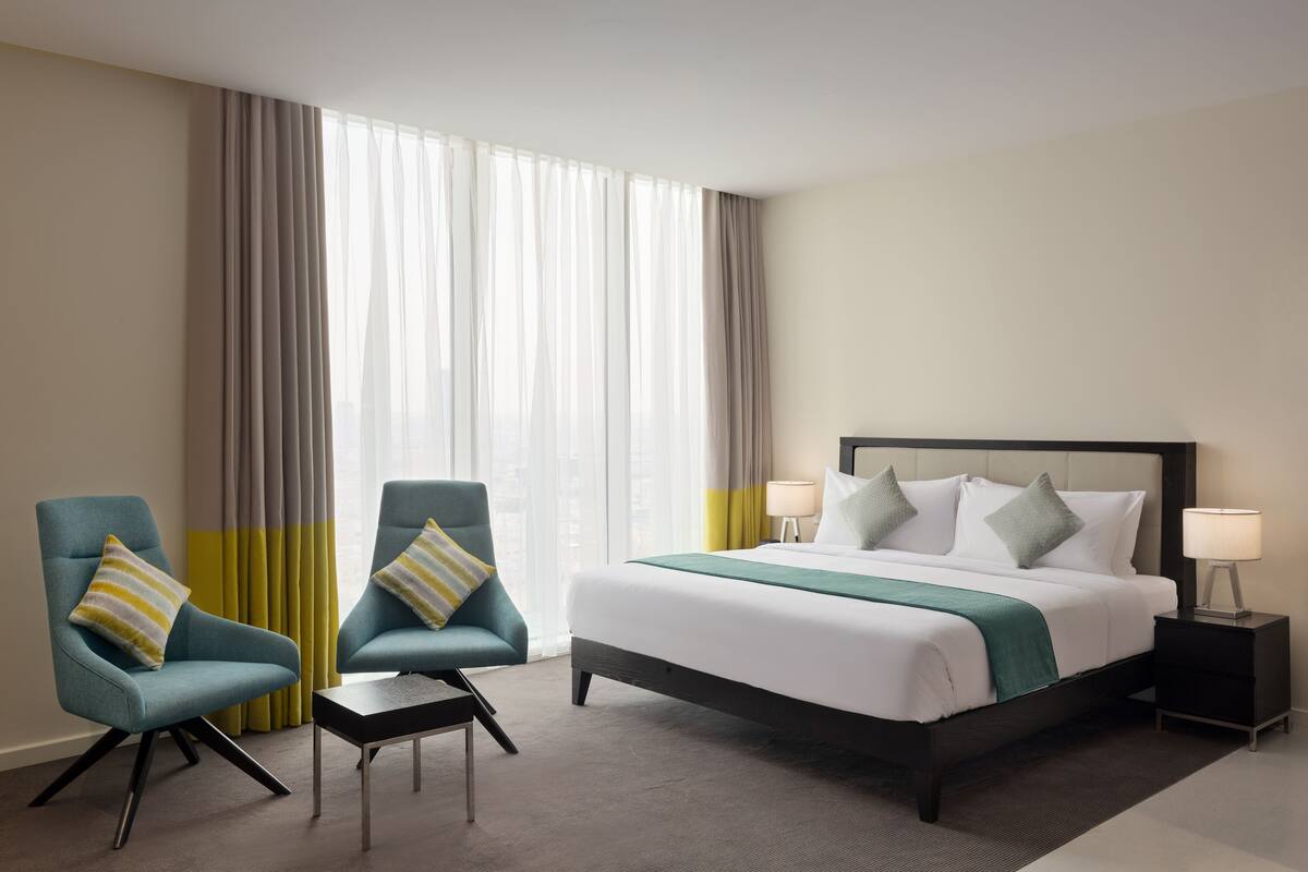 A hotel room with a large bed, two armchairs, a small table, and a nightstand with lamps.