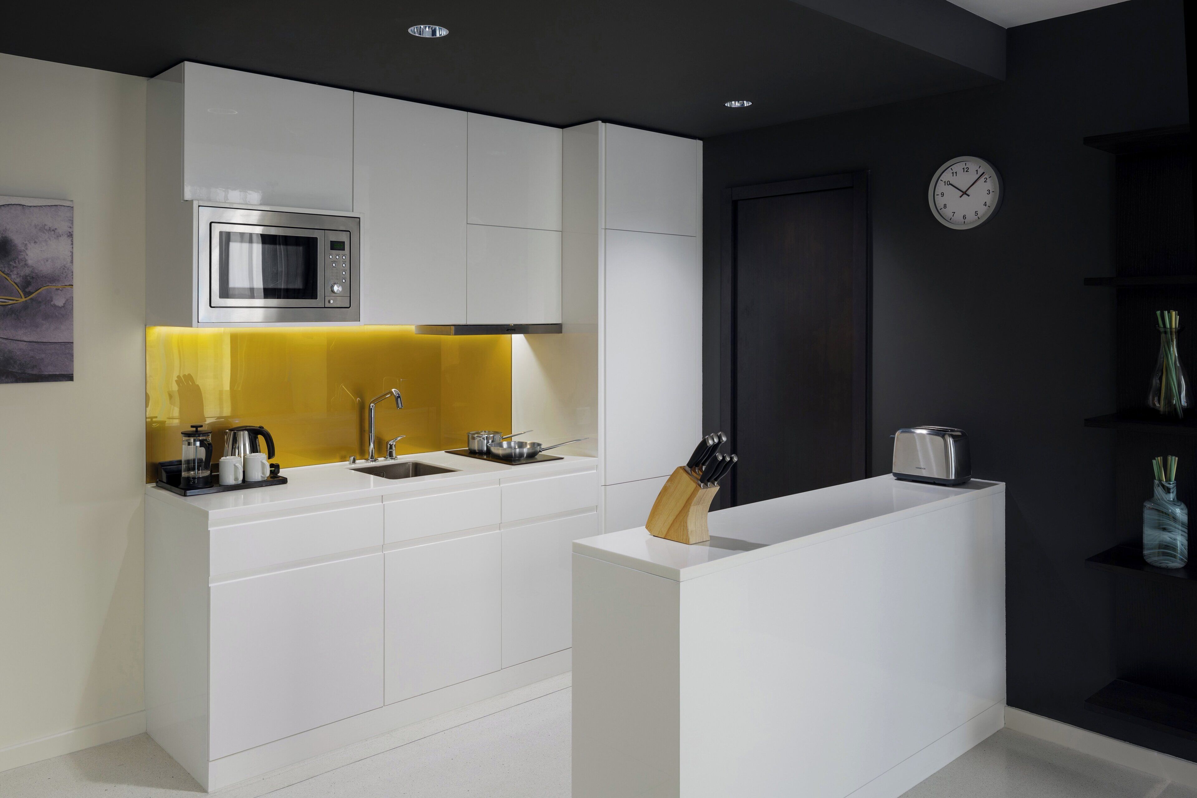 Una cocina moderna con armarios blancos, microondas, lavabo y tostadora.