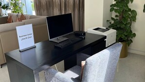 Mesa de centro de negócios com um laptop, teclado e impressora, um aviso indicando o centro de negócios, um sofá e uma planta em vaso.