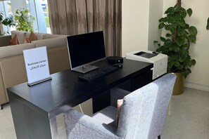 Een bureau voor een business center met een laptop, toetsenbord en printer, een bordje met de naam van het business center, een bank en een potplant.