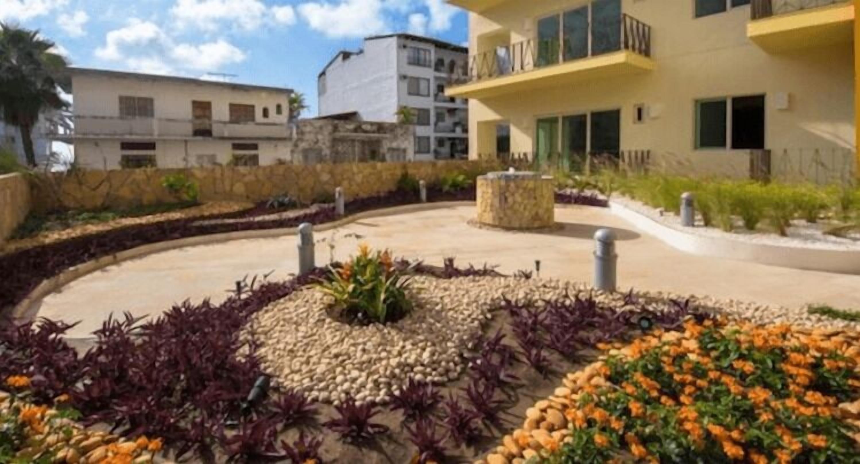 Un patio ajardinado con un parterre circular central, rodeado por un muro de piedra bajo.