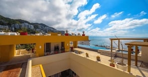 A rooftop terrace with a pool, potted plants, and a view of the sea and mountains.
