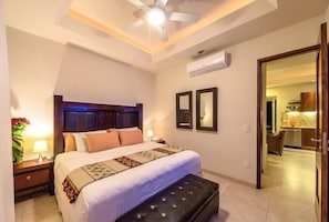 A hotel room with a bed, bedside tables, a ceiling fan, and a view into the adjacent room.