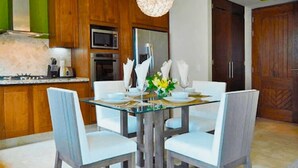 A dining area with a glass table, white chairs, and a chandelier. - Romantic Zone V177 1 Bedroom (Puerto Vallarta)
