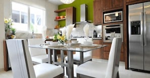 A modern kitchen with a glass dining table, white chairs, stainless steel appliances, and wooden cabinets.