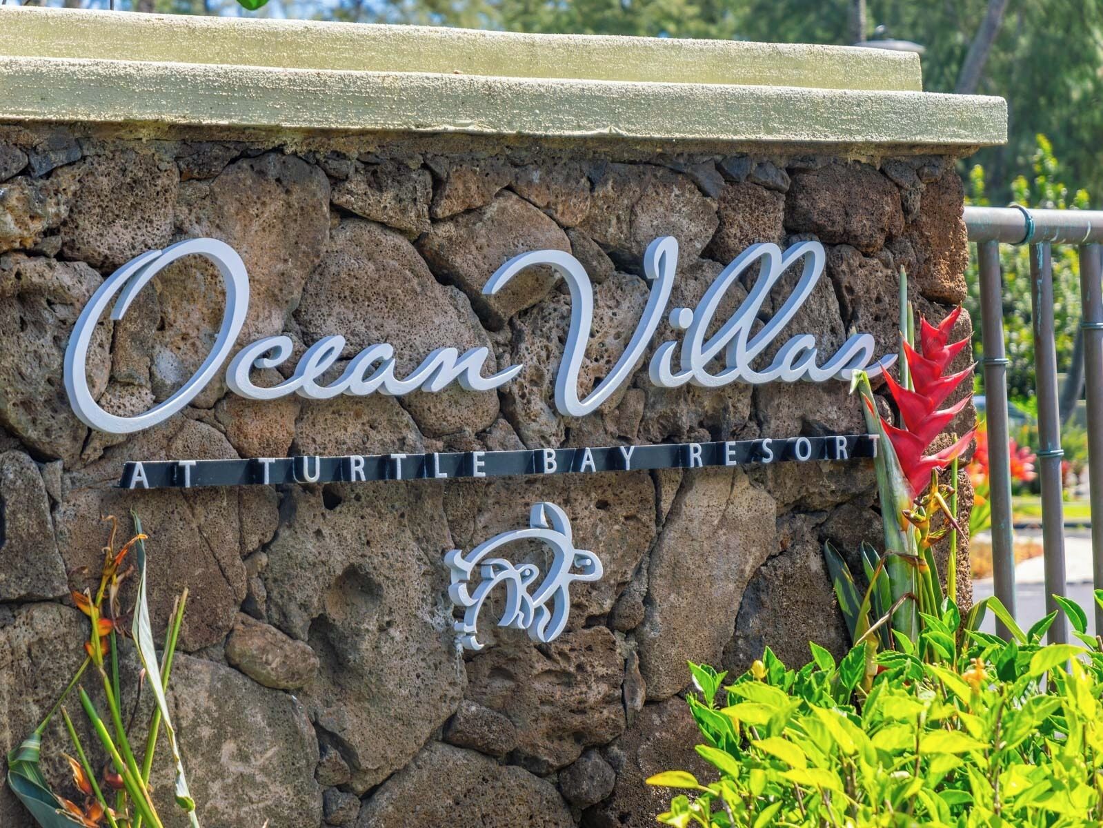 A sign for Ocean Villa at Turtle Bay Resort, featuring a stone wall background and a stylized 'RV' logo.