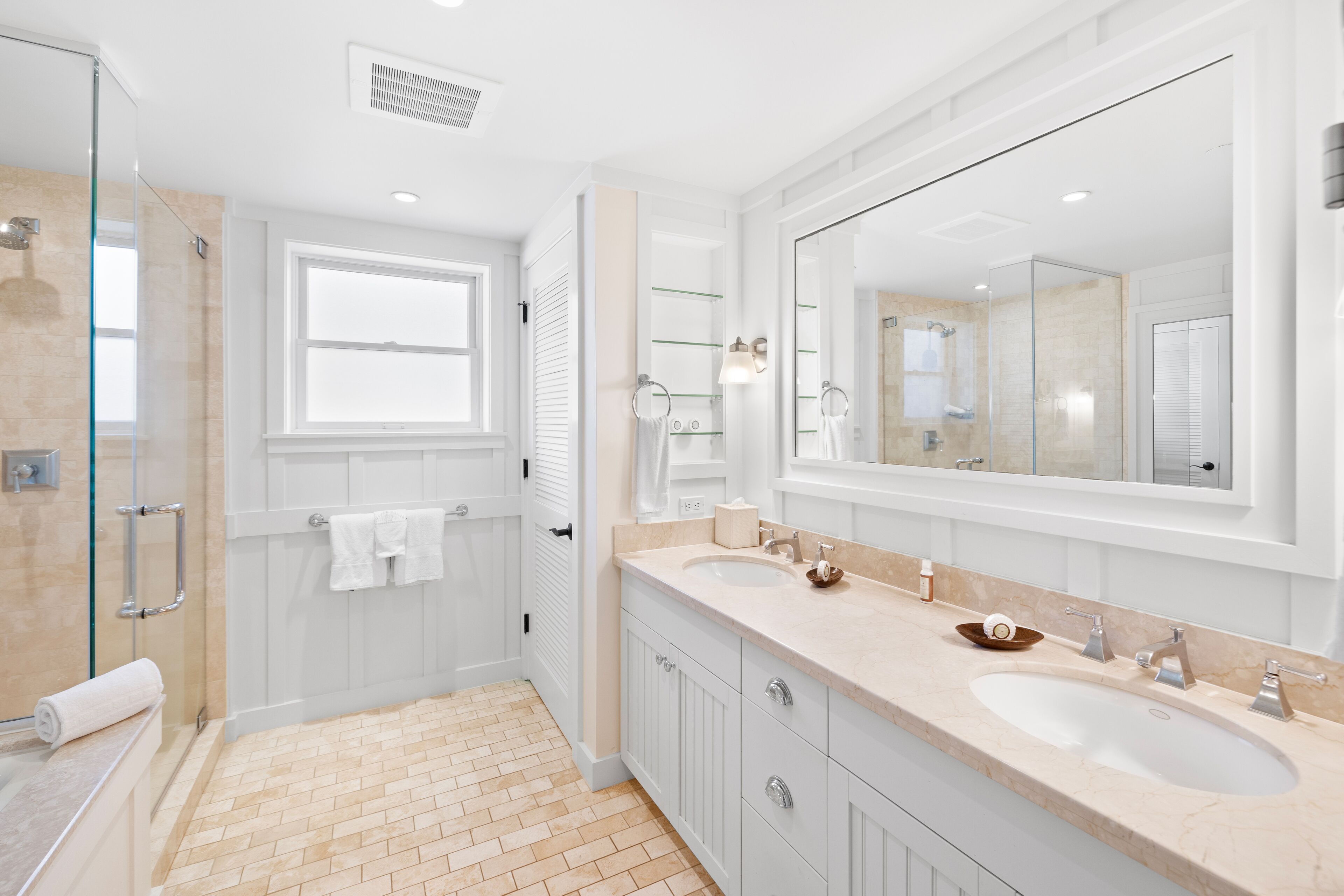 A modern bathroom with two sinks, a large mirror, and a walk-in shower.