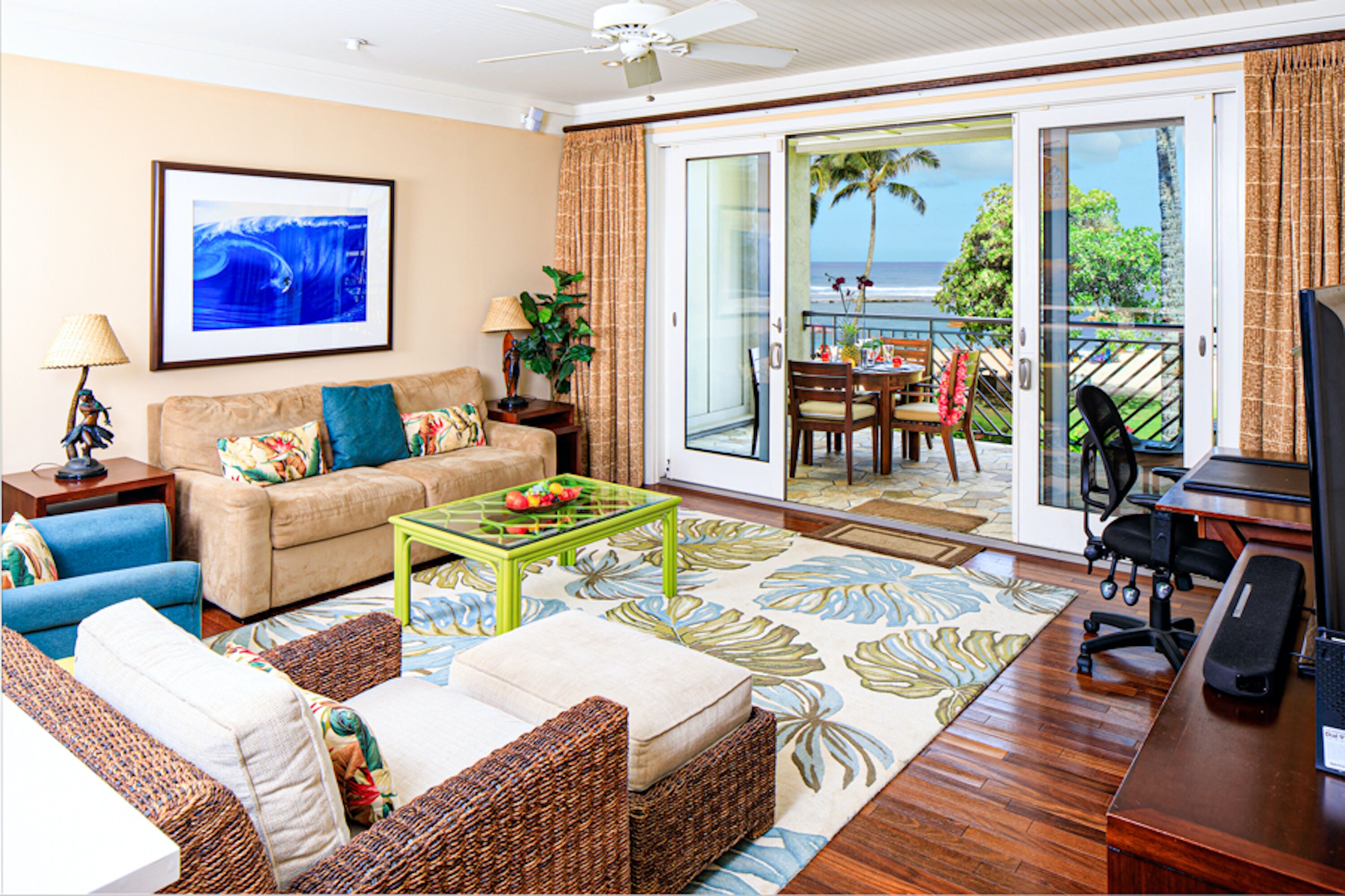 A living room with a sofa, coffee table, and a TV. There is a balcony with a table and chairs.