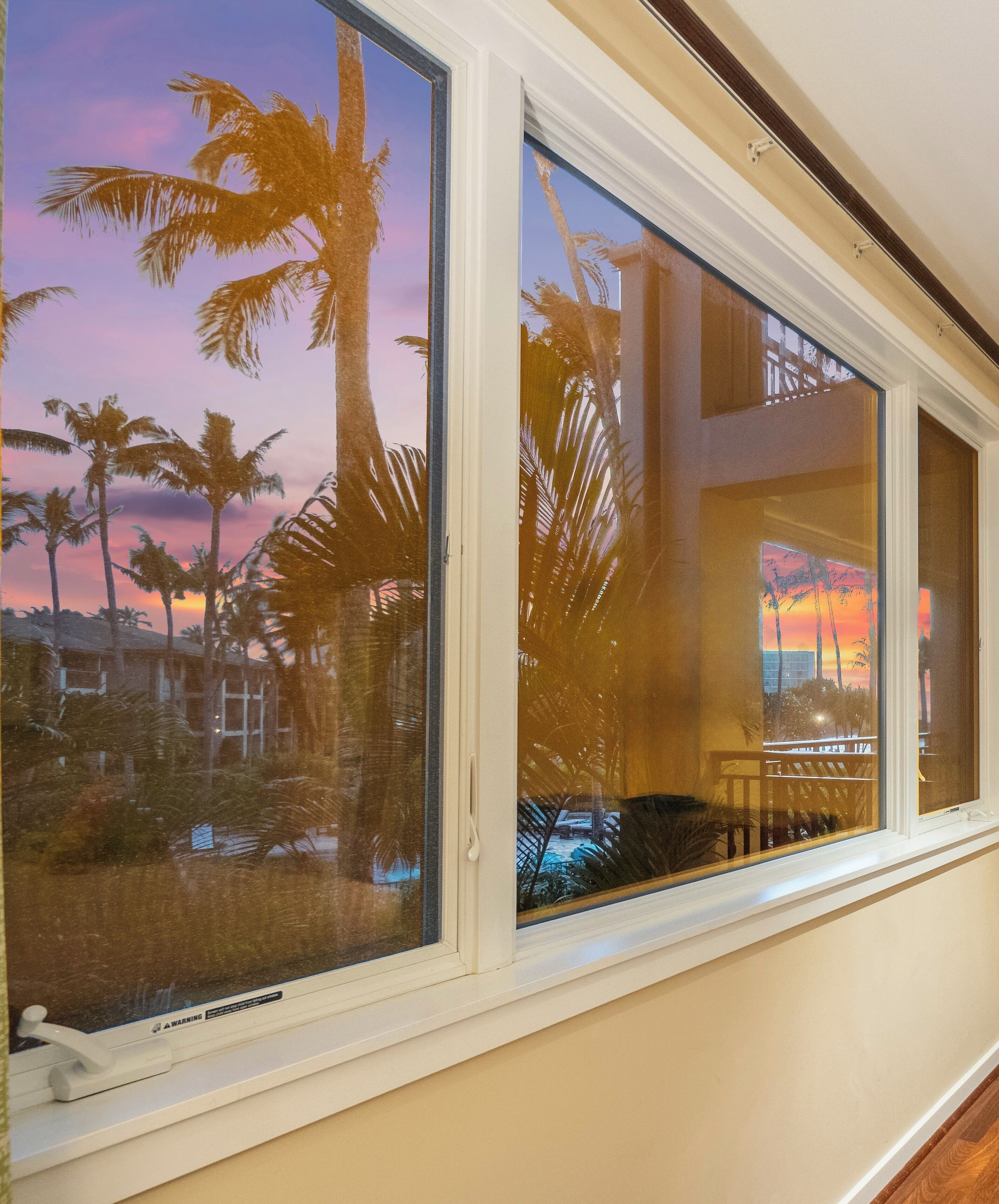 Una ventana con vistas a palmeras y al atardecer.
