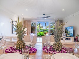 A dining table set with plates, glasses, and two pineapples, with a view of a lush garden and a television in the background.