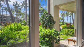 Vista desde una ventana de una habitación de hotel con balcón que da a un jardín exuberante y palmeras.