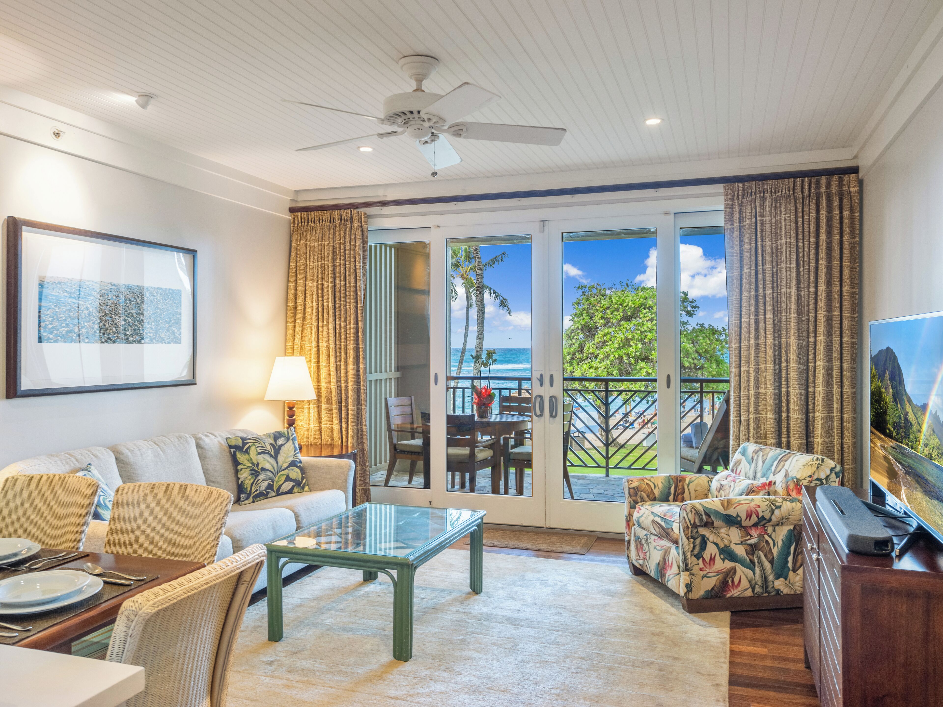 A spacious living area with a glass coffee table, comfortable seating, and a view of the ocean through large sliding doors.