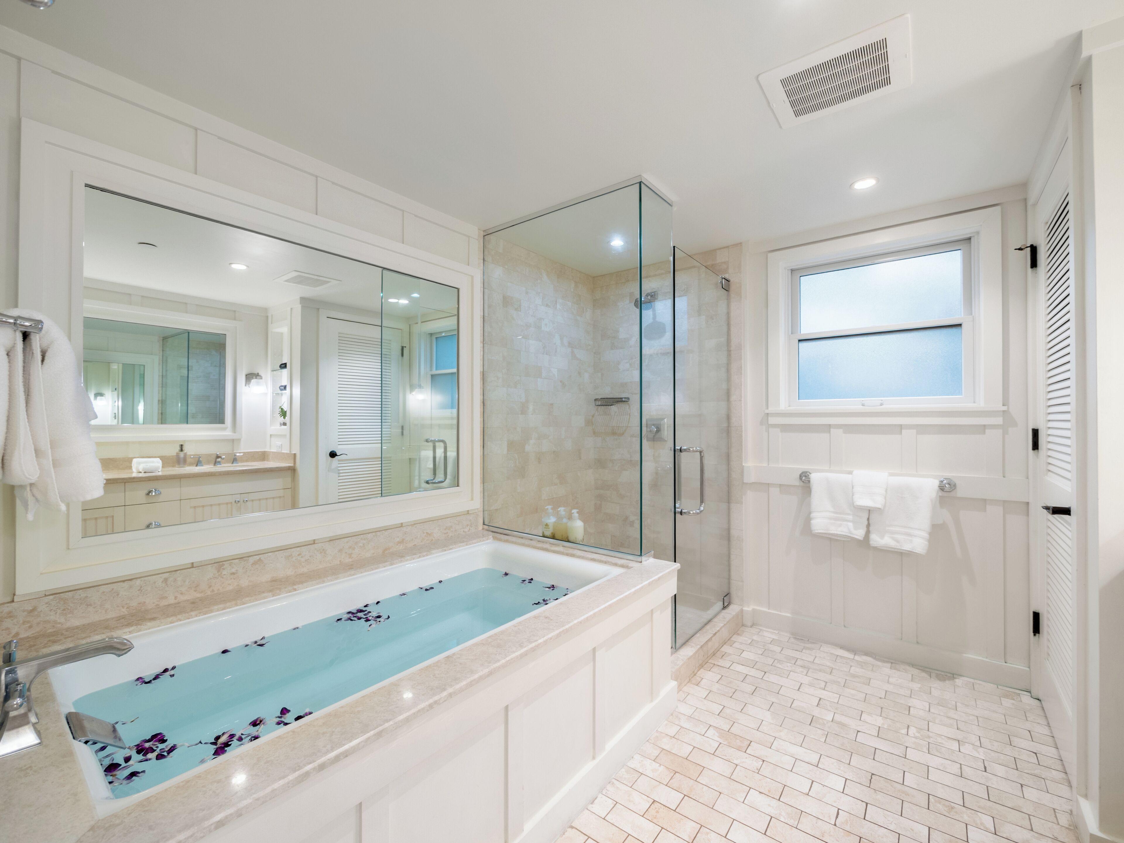 A modern bathroom with a large bathtub, a glass shower enclosure, and a large mirror.