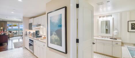 A modern kitchen with white cabinets, a large framed picture, and a view to the living area.