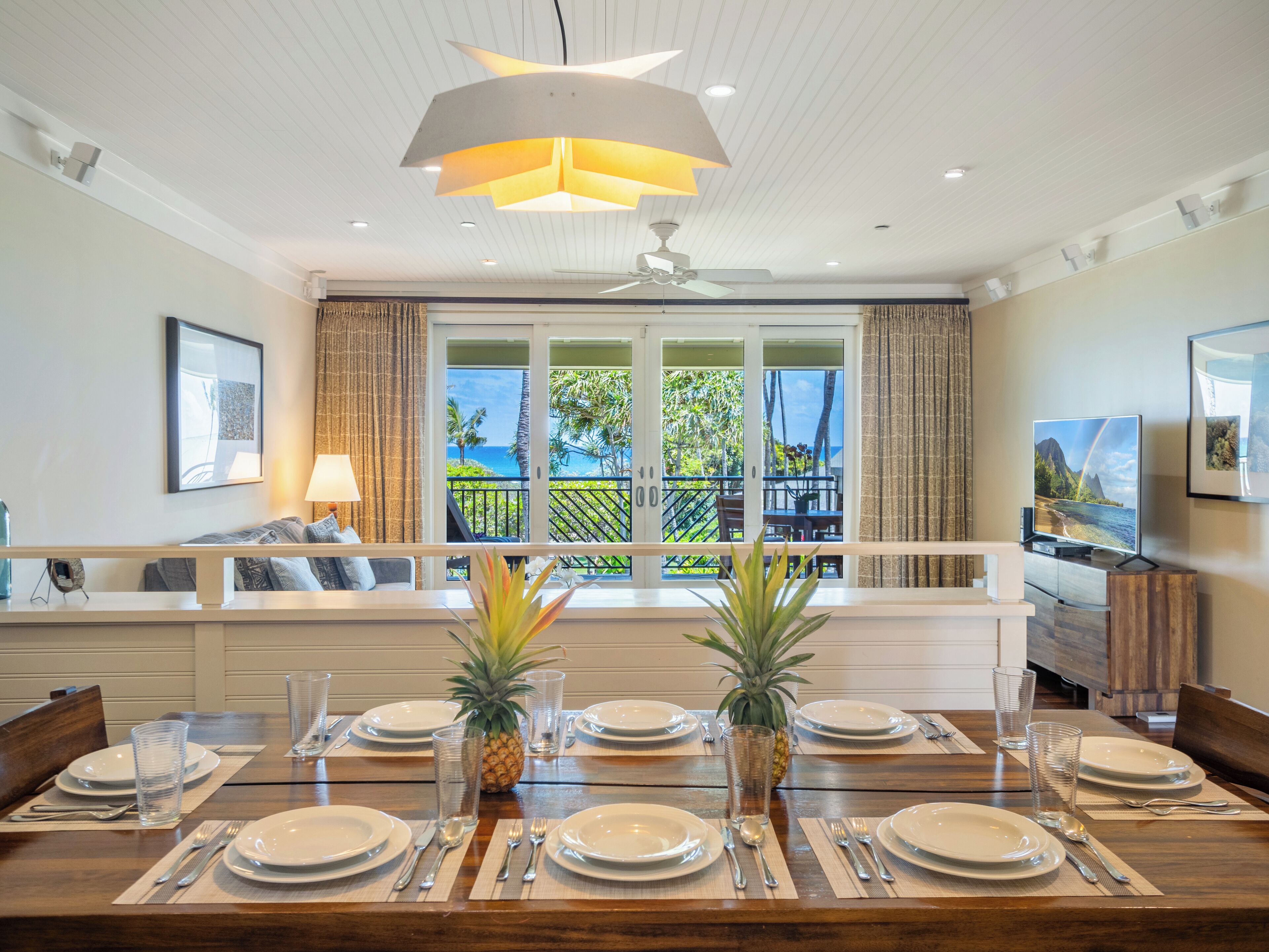 Zona pranzo con vista sull'oceano, ventilatore a soffitto e ampia finestra con tende.