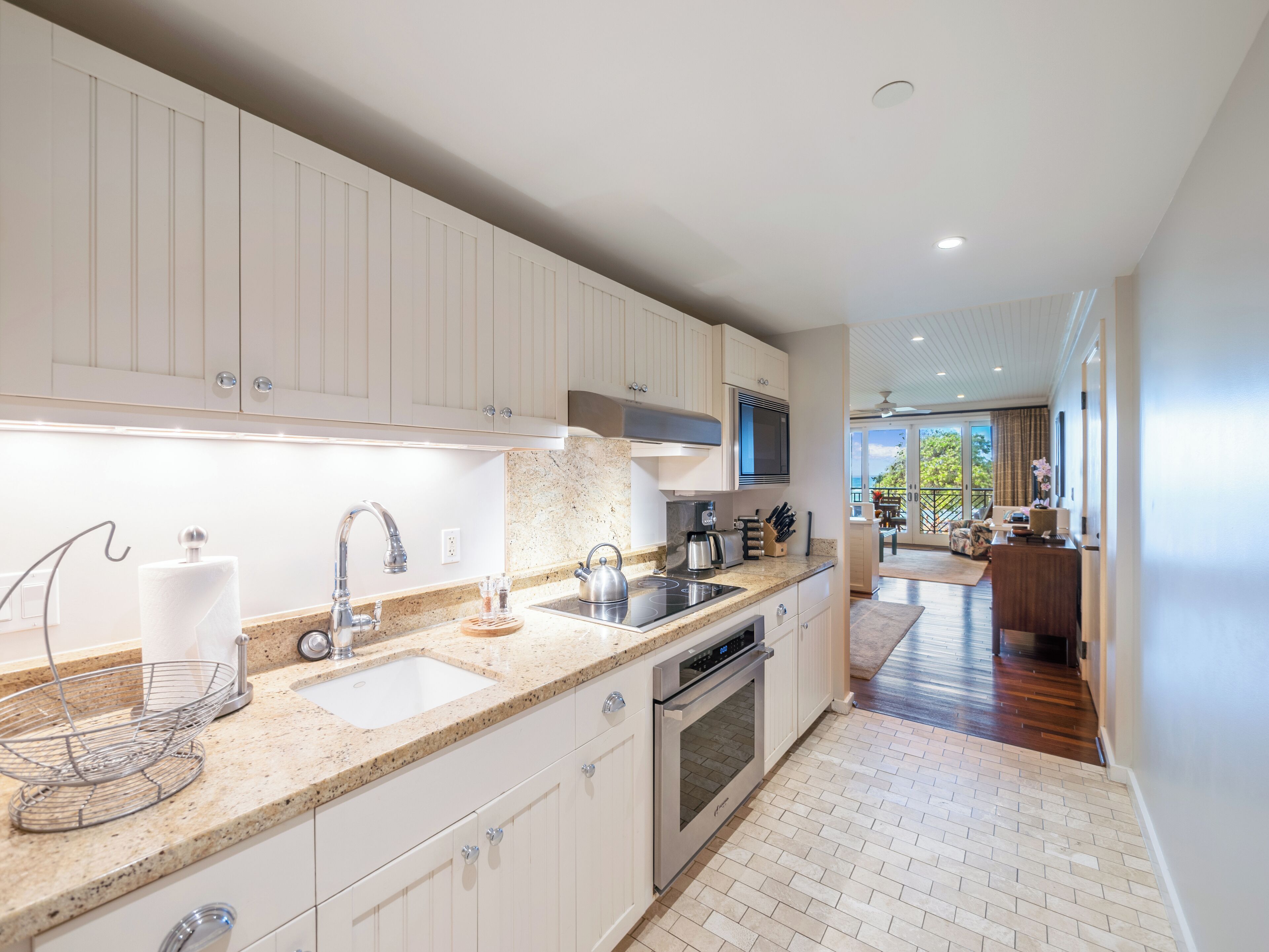 Una cocina moderna con armarios blancos, encimera de granito, electrodomésticos de acero inoxidable y vistas al área de estar.