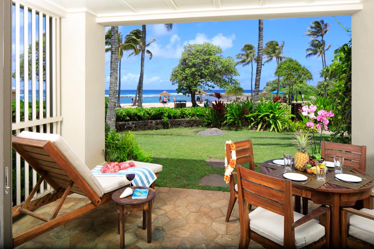Un patio con vista a la playa, una mesa dispuesta con platos, vasos y una piña.