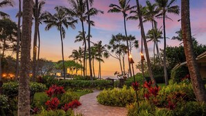 A paved pathway surrounded by lush greenery and tall palm trees, leading towards a scenic view. - Oceanfront Vacation Villas at Turtle Bay (Kahuku)