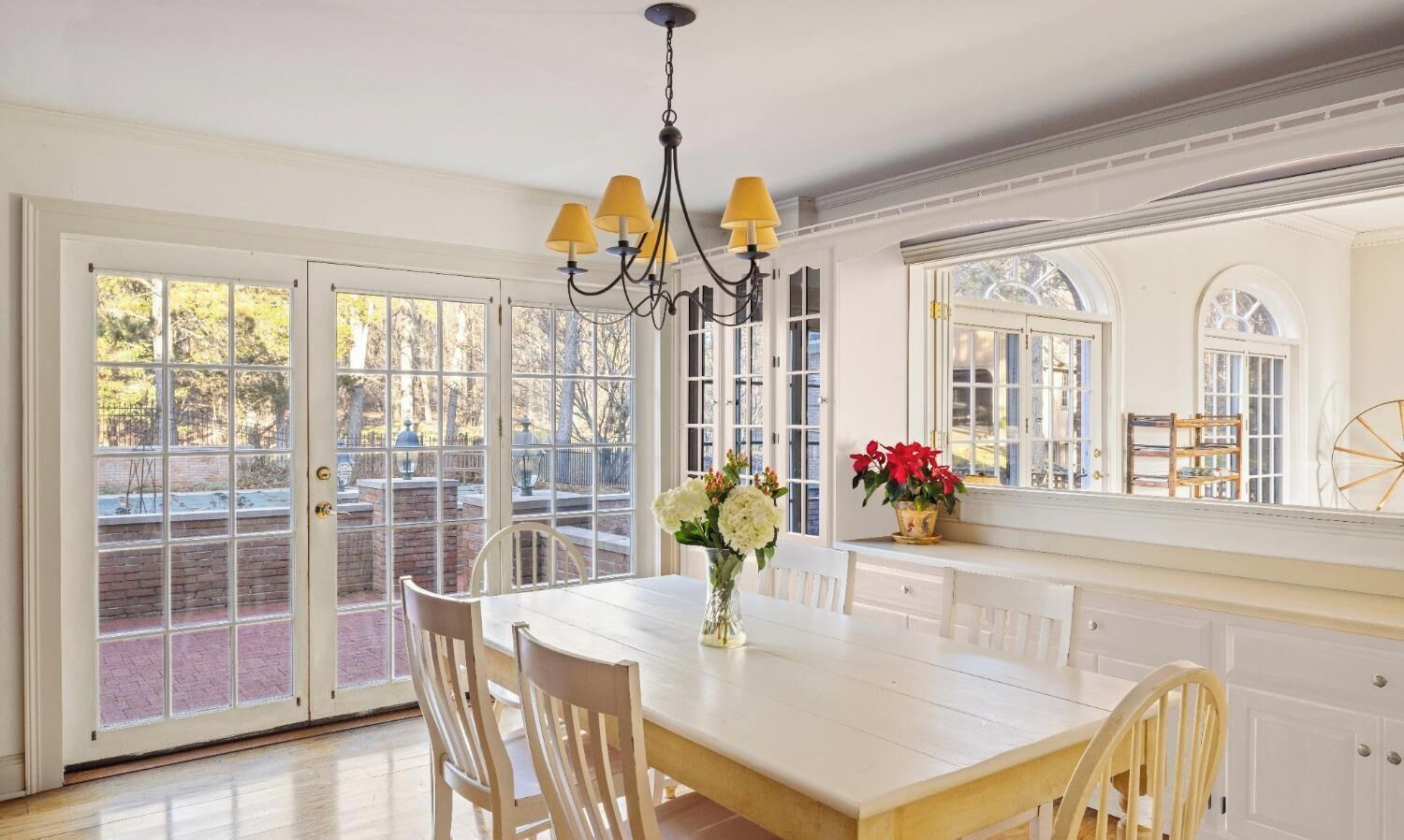 A dining area with a white table and chairs, a chandelier, and a view through large glass doors.
