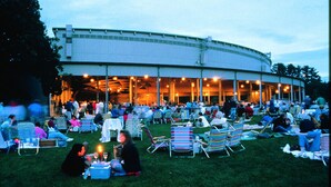 An outdoor gathering area with a large building in the background, surrounded by grass and multiple seating areas.