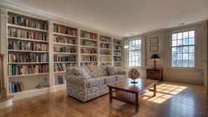 A spacious room with wooden flooring, a large sectional sofa, and multiple bookshelves filled with books.