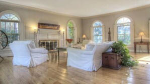 A spacious room with two white upholstered sofas, a fireplace, and large arched windows.