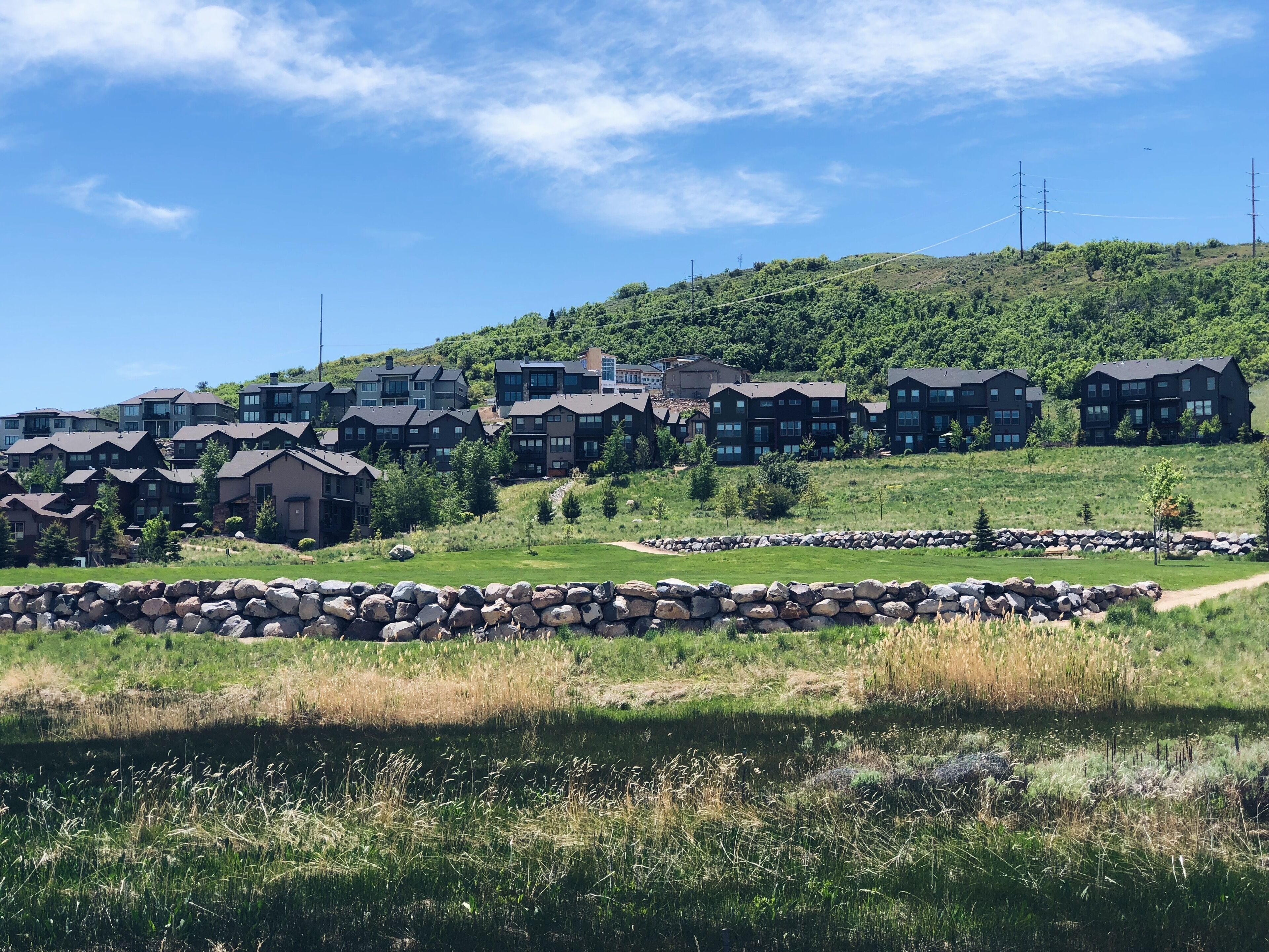 Et boligområde med moderne, h højhus på en skråning, omgivet af grøn vegetation og en stenvæg.