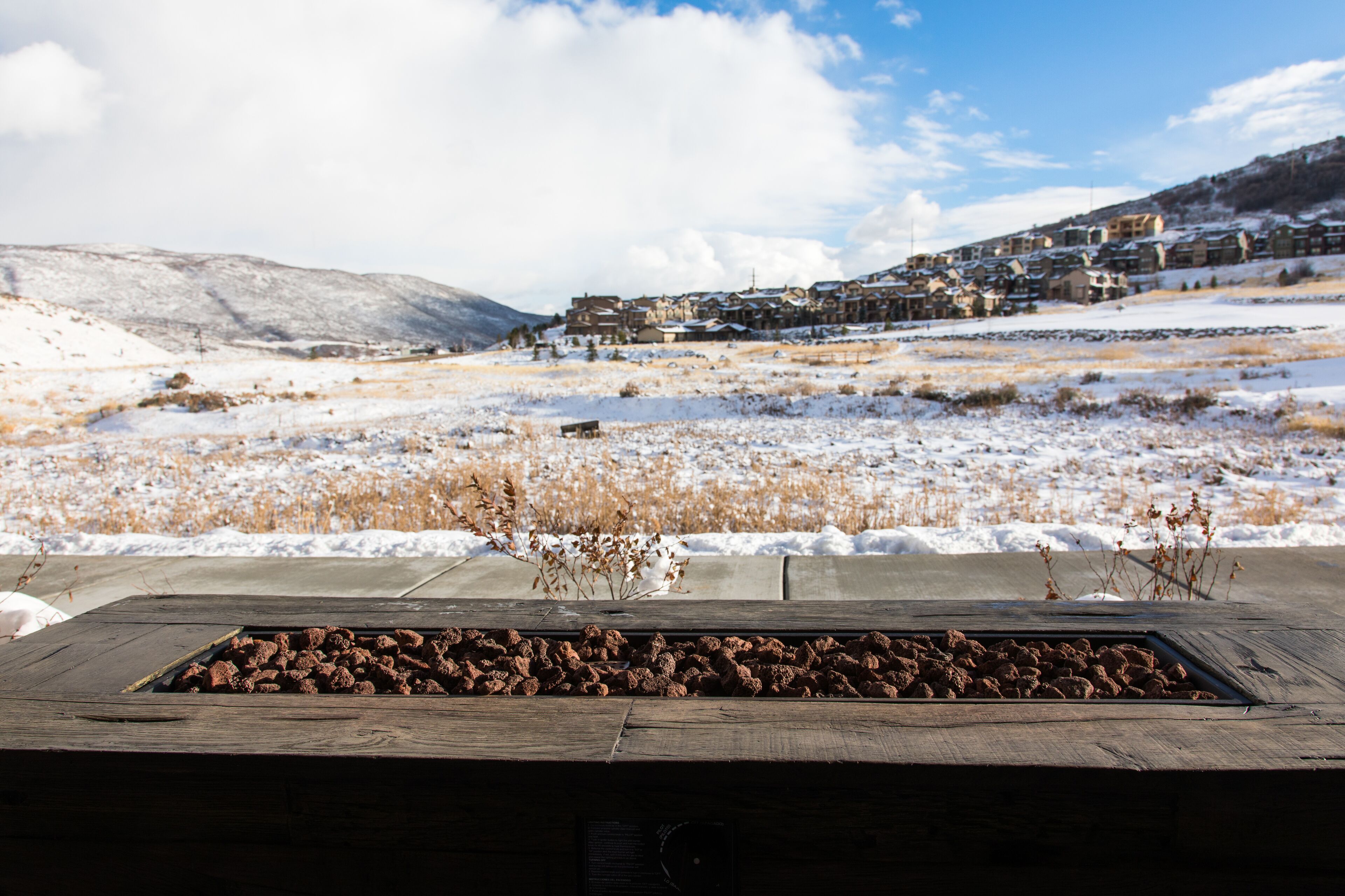 Un paysage enneigé avec un banc en bois et une grille métallique remplie d’objets bruns.