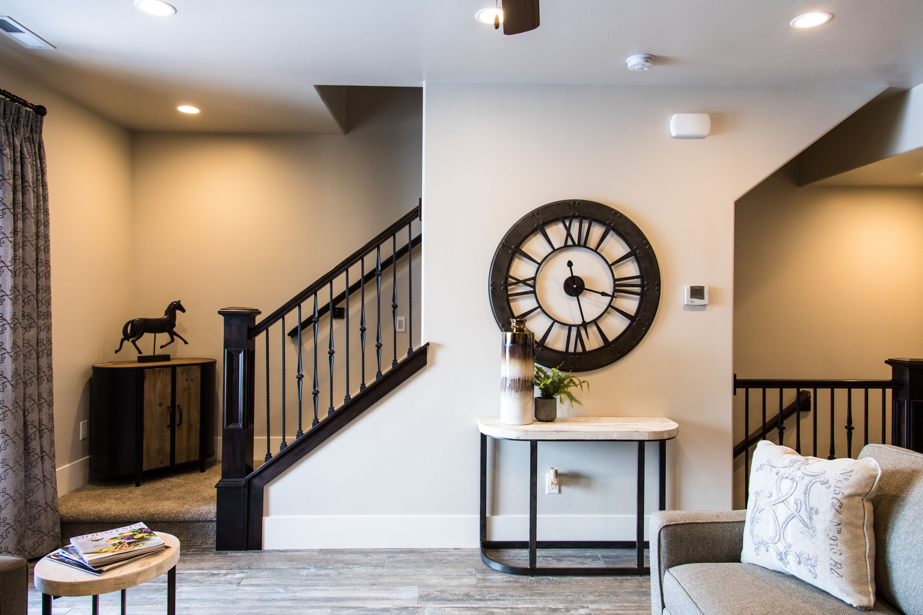 A modern living room with a staircase, a large wall clock, and a decorative horse statue.