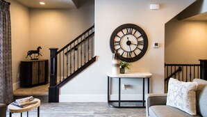 A modern living room with a staircase, a large wall clock, and a decorative horse statue.