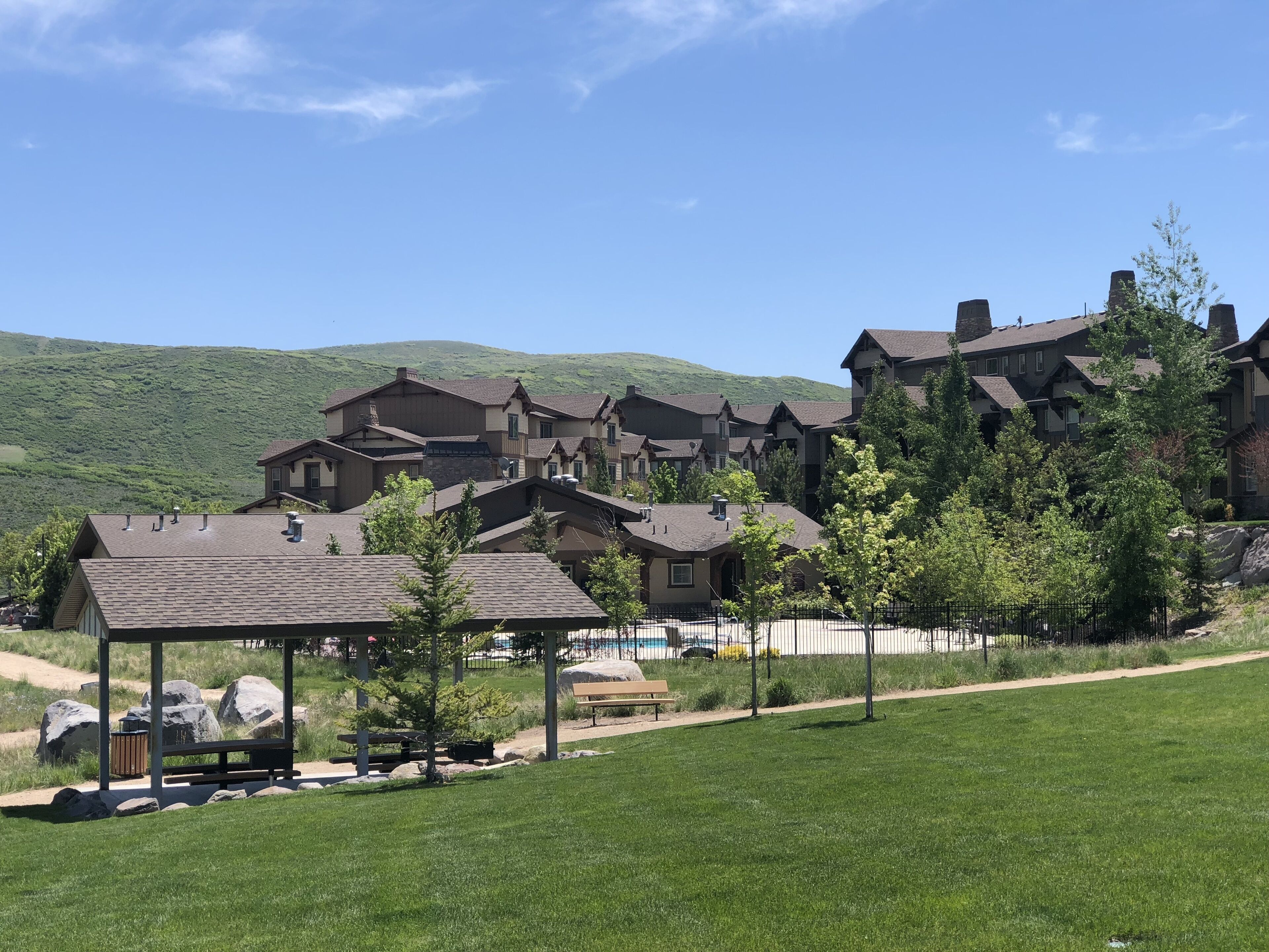A large resort with multiple buildings, a grassy area with a picnic table, and a mountain backdrop.