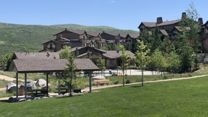 A large resort with multiple buildings, a grassy area with a picnic table, and a mountain backdrop.