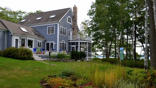 A large house with a wrap-around porch, a stone chimney, and a garden with various plants. - Dramatic Oceanfront House w/ Private Swimming Cove & Dock (Freeport)