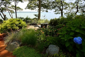 A garden with a bench, a table, and chairs overlooking a body of water.